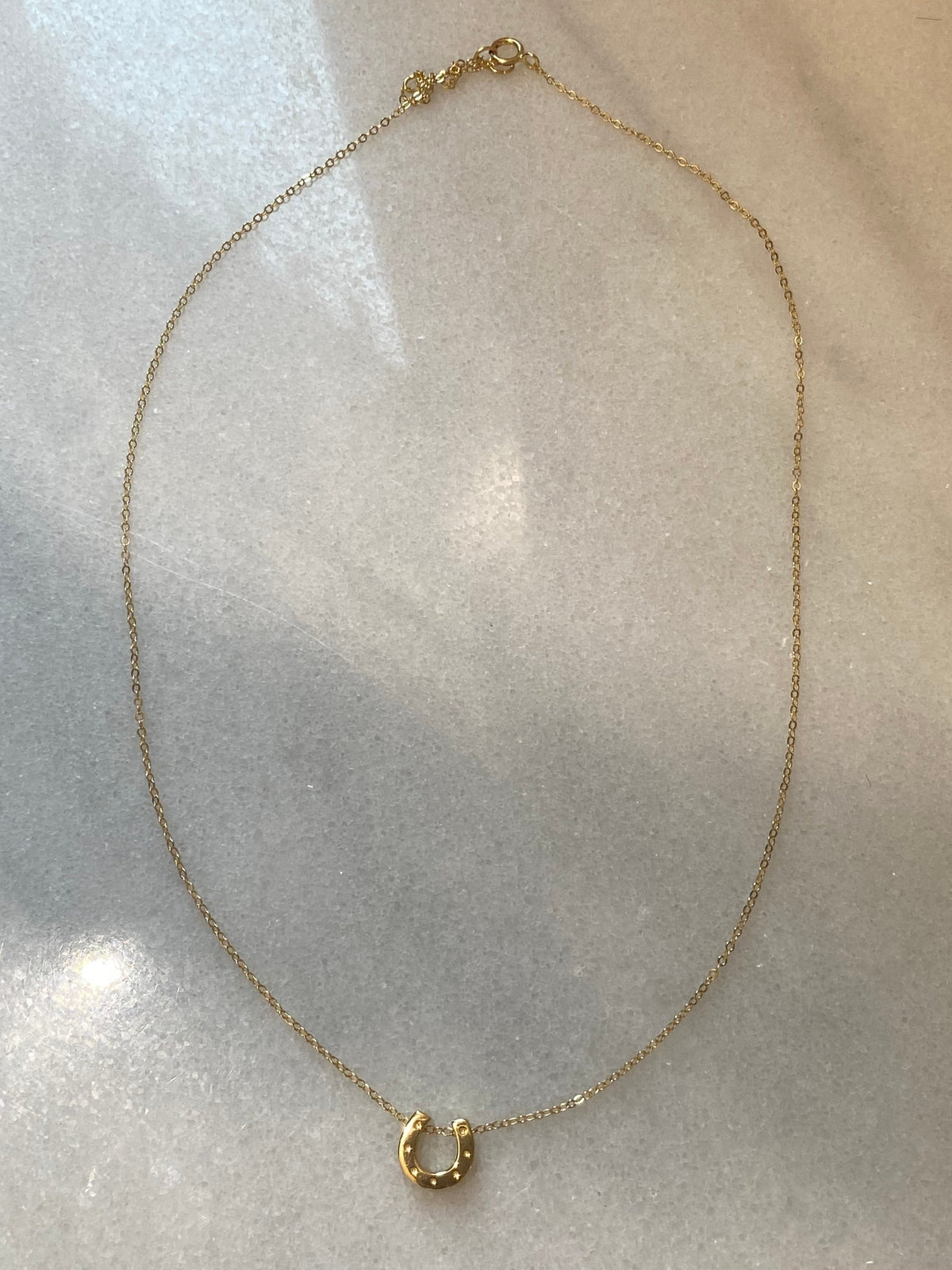 A delicate gold chain necklace with a small textured gold hoop pendant, displayed on a light gray textured surface.